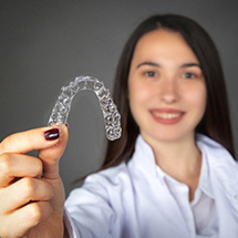 A young woman holding a clear Invisalign aligner in her right hand