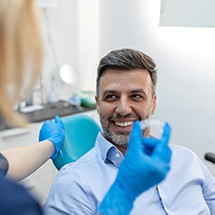 Patient smiling at dentist who is holding clear aligner with blue gloves