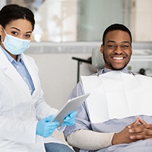 Patient smiling next to dentist holding tablet