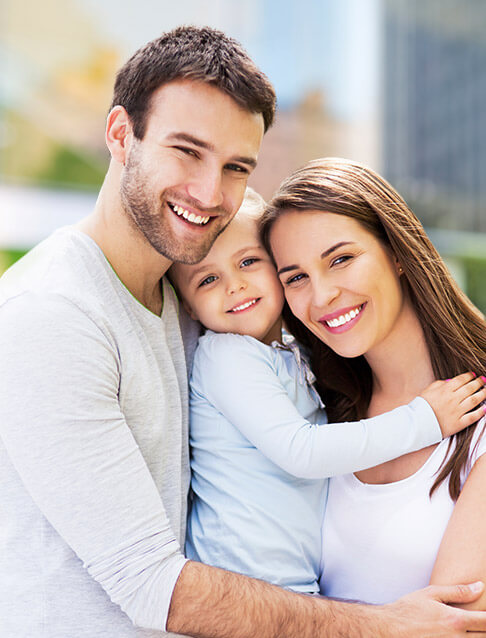 Family of three sharing healthy smiles after preventive dentistry