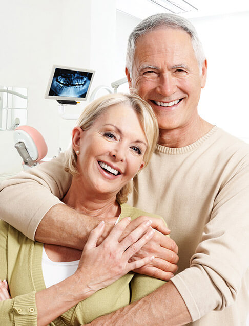 Older couple smiling after replacing missing teeth